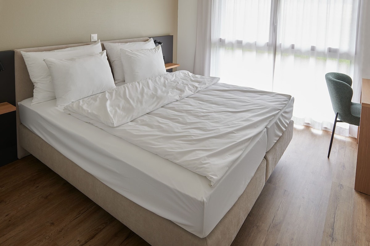 A neatly made bed with white linens in a modern hotel room.