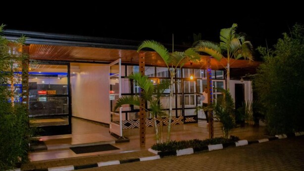A modern building with a glass facade, a covered outdoor seating area, and a well-maintained garden with palm trees. - Boutique Hotel Rwanda (Kigali)