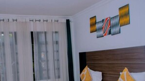 A hotel room with a large bed, white bedding, and a red throw blanket. There is a wooden headboard and two decorative pillows. - Boutique Hotel Rwanda (Kigali)