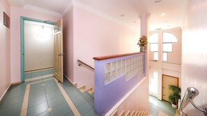 A hallway with a teal and beige tiled floor, a wooden door, and a staircase with a blue railing. - Hotel Famous Inn (Malacca City)
