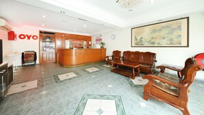 A hotel lobby with a reception desk, wooden seating, a chandelier, and a painting on the wall. - Hotel Famous Inn (Malacca City)