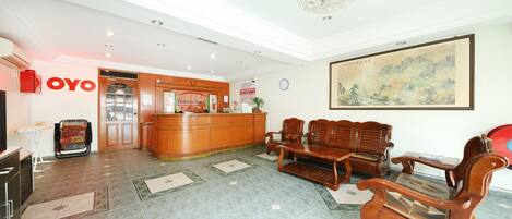 A hotel lobby with a reception desk, wooden seating, a chandelier, and a painting on the wall.