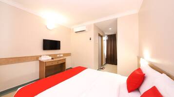 A hotel room with a bed, a TV mounted on the wall, a desk with a chair, and a bathroom visible through an open door.