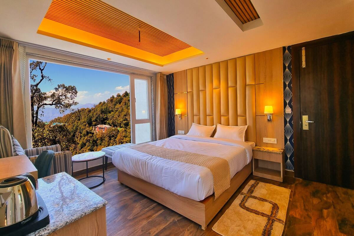 Una habitación de hotel moderna con una cama grande, un escritorio con hervidor, vistas al exterior y un cabecero de madera.
