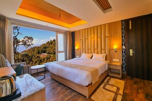 Ein modernes Hotelzimmer mit einem großen Bett, einem Schreibtisch mit Wasserkocher, Blick ins Freie und einem Holzkopfende.