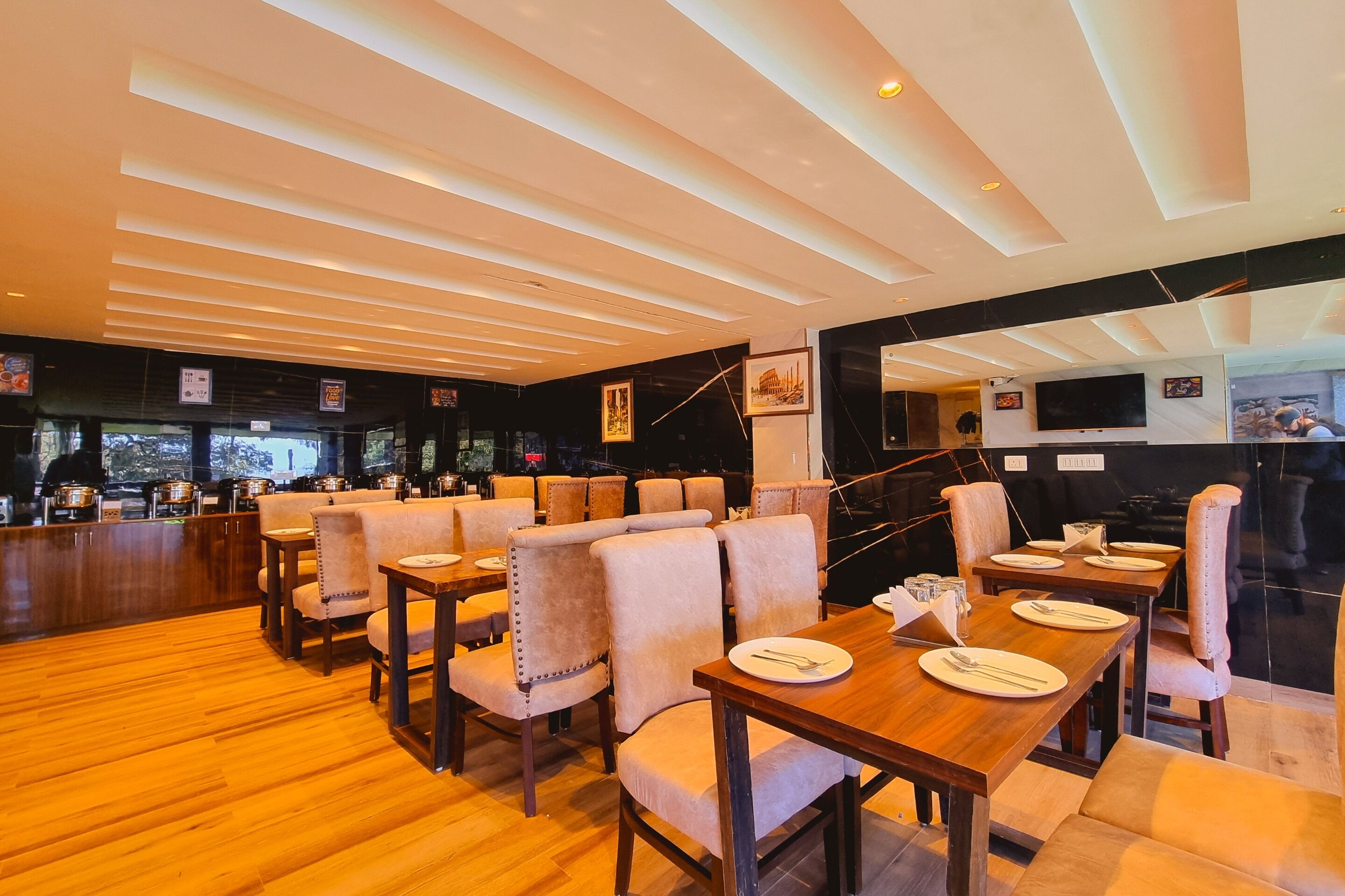 A restaurant with wooden tables and cushioned chairs, a bar area, and a large TV screen.