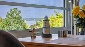 Blick durch ein Fenster mit einem Leuchtturm-Modell, einer Vogel-Figur und einer Vase mit gelben Blumen.