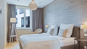 A modern hotel room with a large bed, a side table, a chair, and a view of the city through the window.