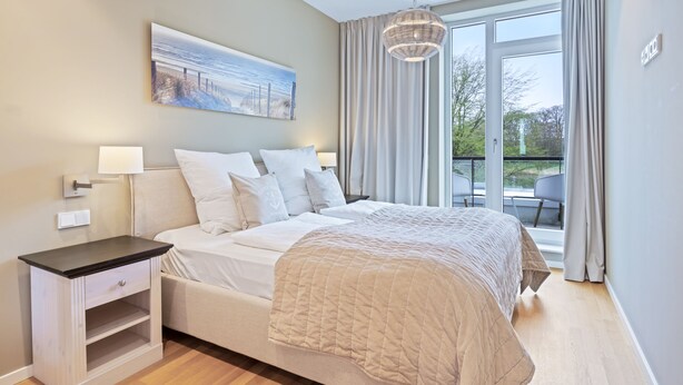 A bedroom with a bed, bedside tables, a painting, and a view of the outdoors.
