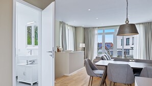 A modern kitchen with white cabinets and a window, a dining area with a table and chairs, and a view of buildings outside.
