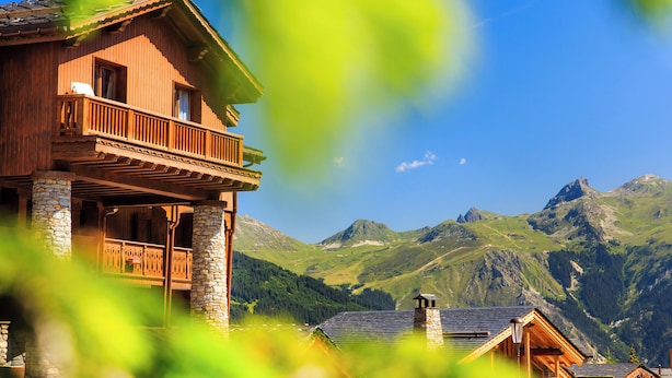 A wooden chalet with a balcony, stone pillars, and a mountain backdrop. - Hotel Blanche Neige   (Courchevel)