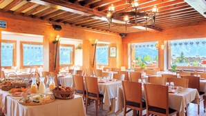 A restaurant with wooden interiors, multiple tables set for dining, and large windows offering mountain views. - Hotel Blanche Neige   (Courchevel)