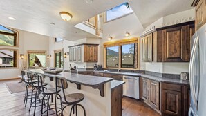 A spacious kitchen with a large island, wooden cabinets, and bar stools. - Ski-in/Ski-Out with Private Hot Tub (Whitefish)