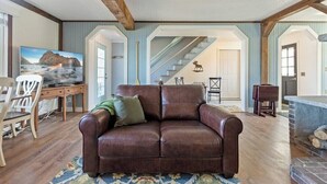 Ein Wohnzimmer mit braunem Ledersofa, Holzboden, einem Fernseher und einer Treppe, die in einen anderen Raum führt.