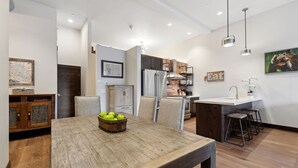Een moderne keuken met een eethoek, met een houten tafel, een fruitschaal, een koelkast en een spoelbak met krukken.