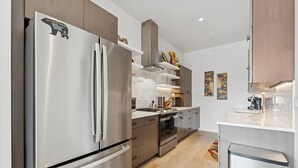 Una cocina moderna con electrodomésticos de acero inoxidable, armarios de madera y una encimera blanca.