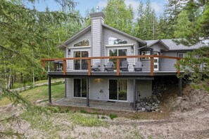 A modern two-story house with a covered deck and a stone foundation. - Book a Ski Stay! Luxury! Stunning Home with Amazing Views and Hot Tub! (Whitefish)