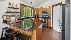 Een moderne keuken met een centraal eiland, houten kasten, een roestvrijstalen koelkast en een groot raam voor natuurlijk licht.