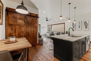 Een moderne keuken met een houten eettafel, een groot keukeneiland met een spoelbak en hangende lampen.