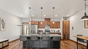A modern kitchen with wooden cabinets, a central island with bar stools, stainless steel appliances, and pendant lighting. - Luxury Condo in Downtown with Fireplace (Whitefish)