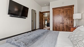 A bedroom with a bed, a TV mounted on the wall, a wooden wardrobe, and a mirror. - Luxury Condo in Downtown with Fireplace (Whitefish)