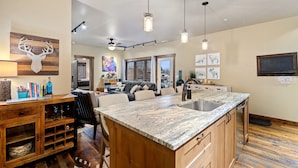 A spacious living area with a large island kitchen, wooden cabinetry, and a ceiling fan.