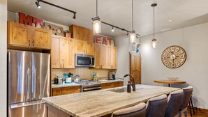A modern kitchen with wooden cabinets, stainless steel appliances, a central island with bar stools, and a wall clock.