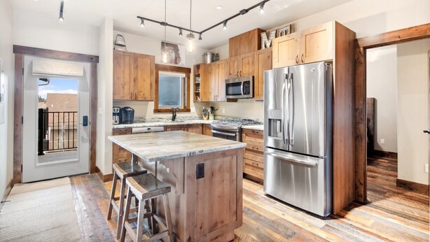 A modern kitchen with wooden cabinets, stainless steel appliances, and a central island with bar stools. - Penthouse with Hot Tub and Fire Table (Whitefish)