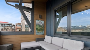 A balcony with a wicker sofa, a small table, and a poster of Glacier National Park.