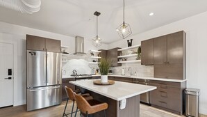 A modern kitchen with stainless steel appliances, a central island with stools, and a decorative plant.