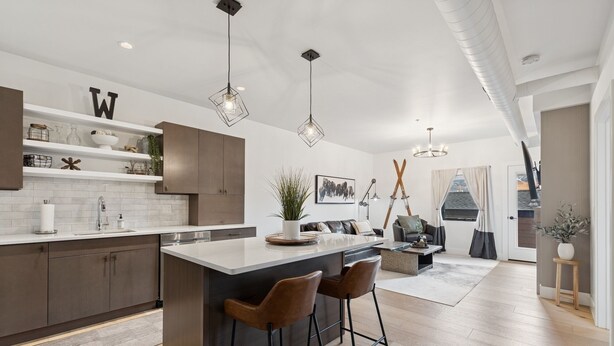 A modern kitchen with a central island, bar stools, and pendant lighting.