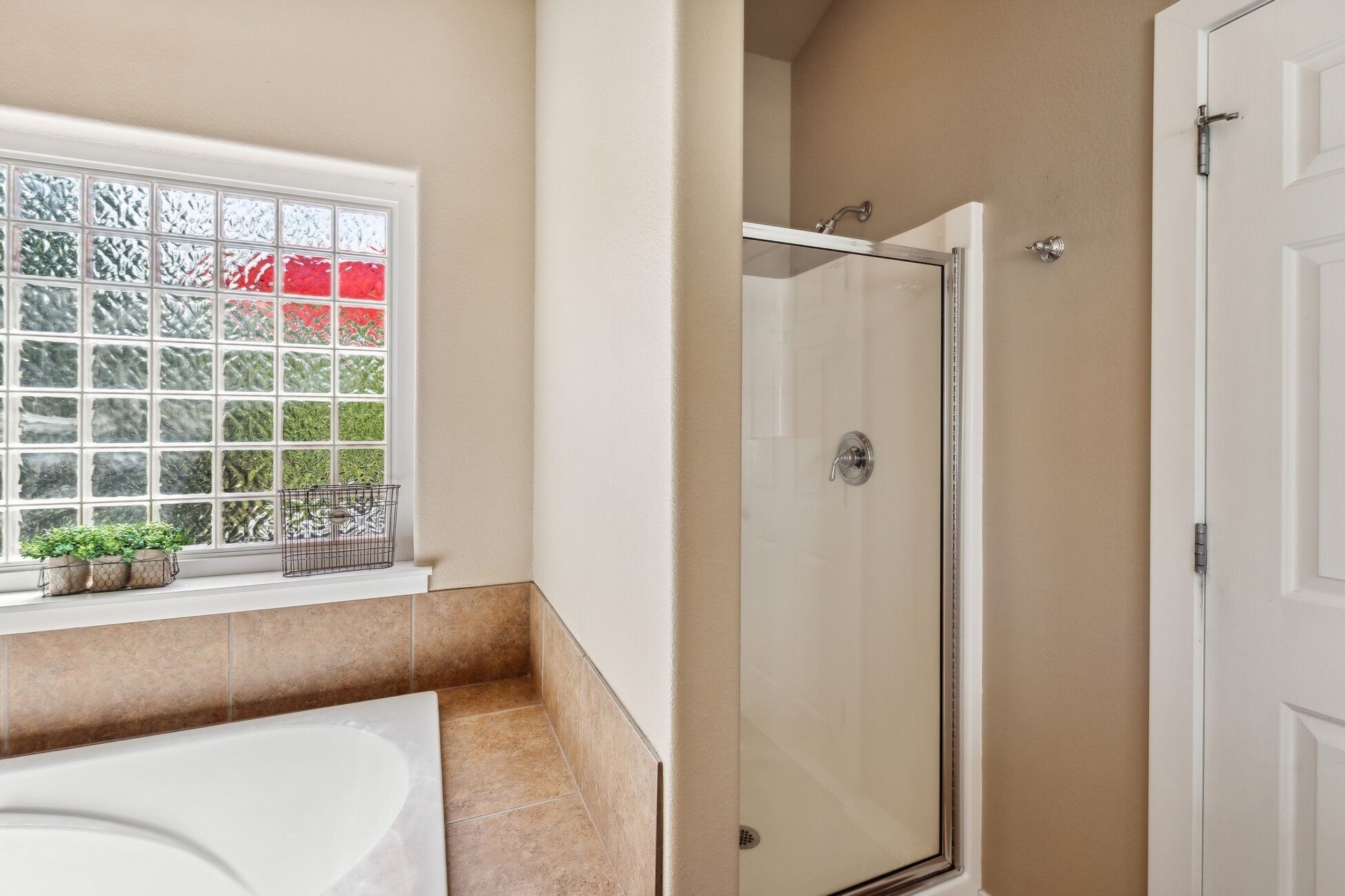 A bathroom with a glass shower enclosure, a bathtub, and a window with a view of greenery.