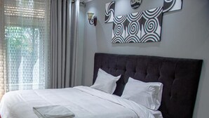 Quarto com cabeceira escura, roupa de cama branca e uma obra de arte geométrica na parede.