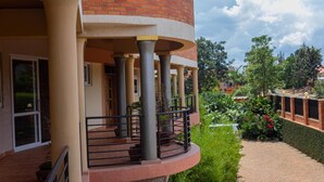 Um edifício com uma seção circular de tijolos, uma varanda com guarda-corpo de metal e um caminho pavimentado com vegetação.