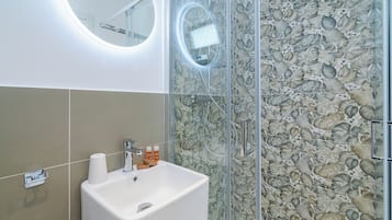 A bathroom with a white sink, a mirror, and a glass shower enclosure with a floral tile design.
