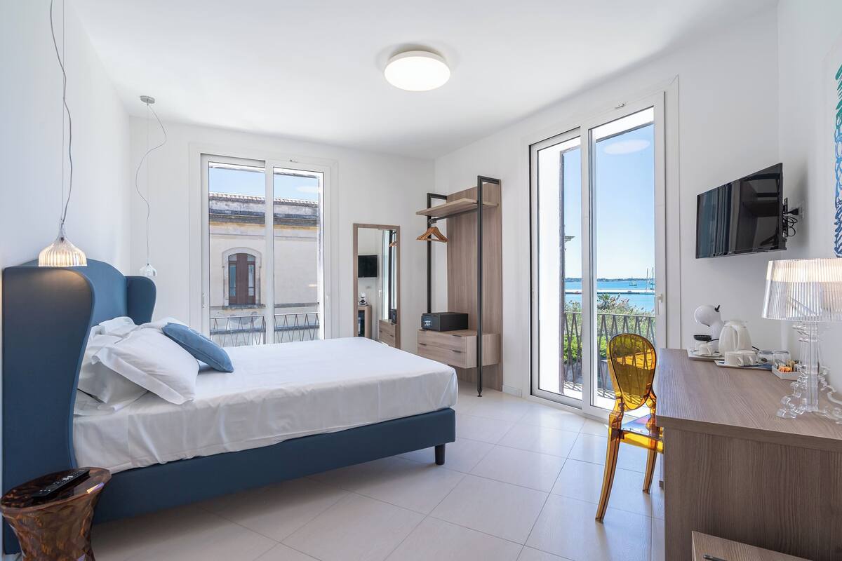 Ein modernes Schlafzimmer mit einem großen Bett, einem Schreibtisch mit Stuhl, einem Fernseher und einem Balkon mit Blick.