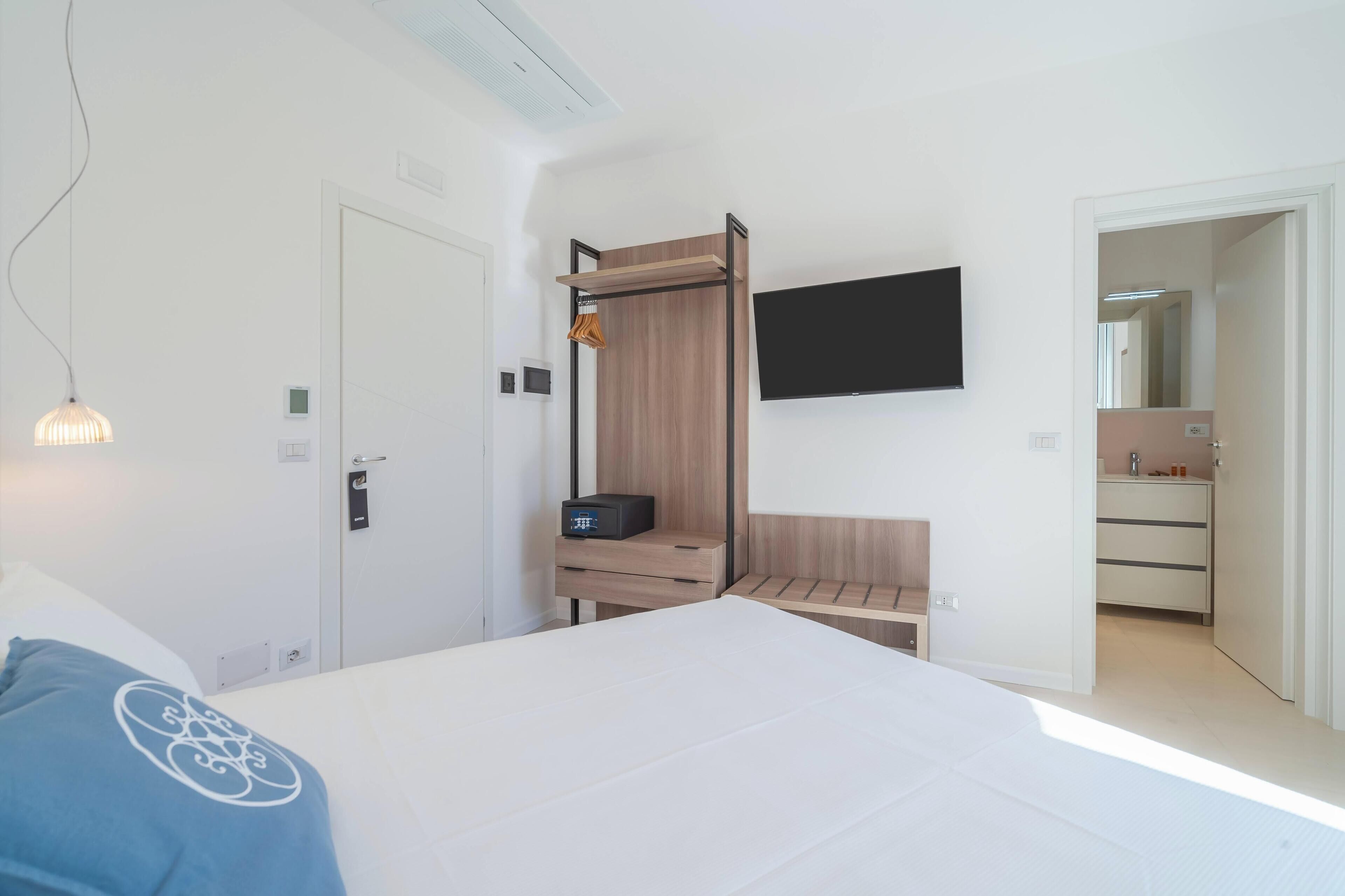 Une chambre à coucher moderne avec un lit, un téléviseur fixé au mur, une armoire en bois et un bureau avec une lampe.