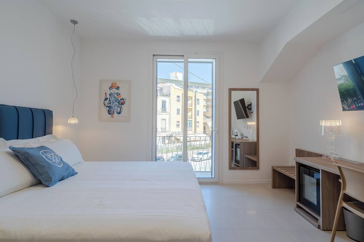 Ein modernes Schlafzimmer mit einem großen Bett, einem Fernseher und einem Balkon mit Blick auf Gebäude.