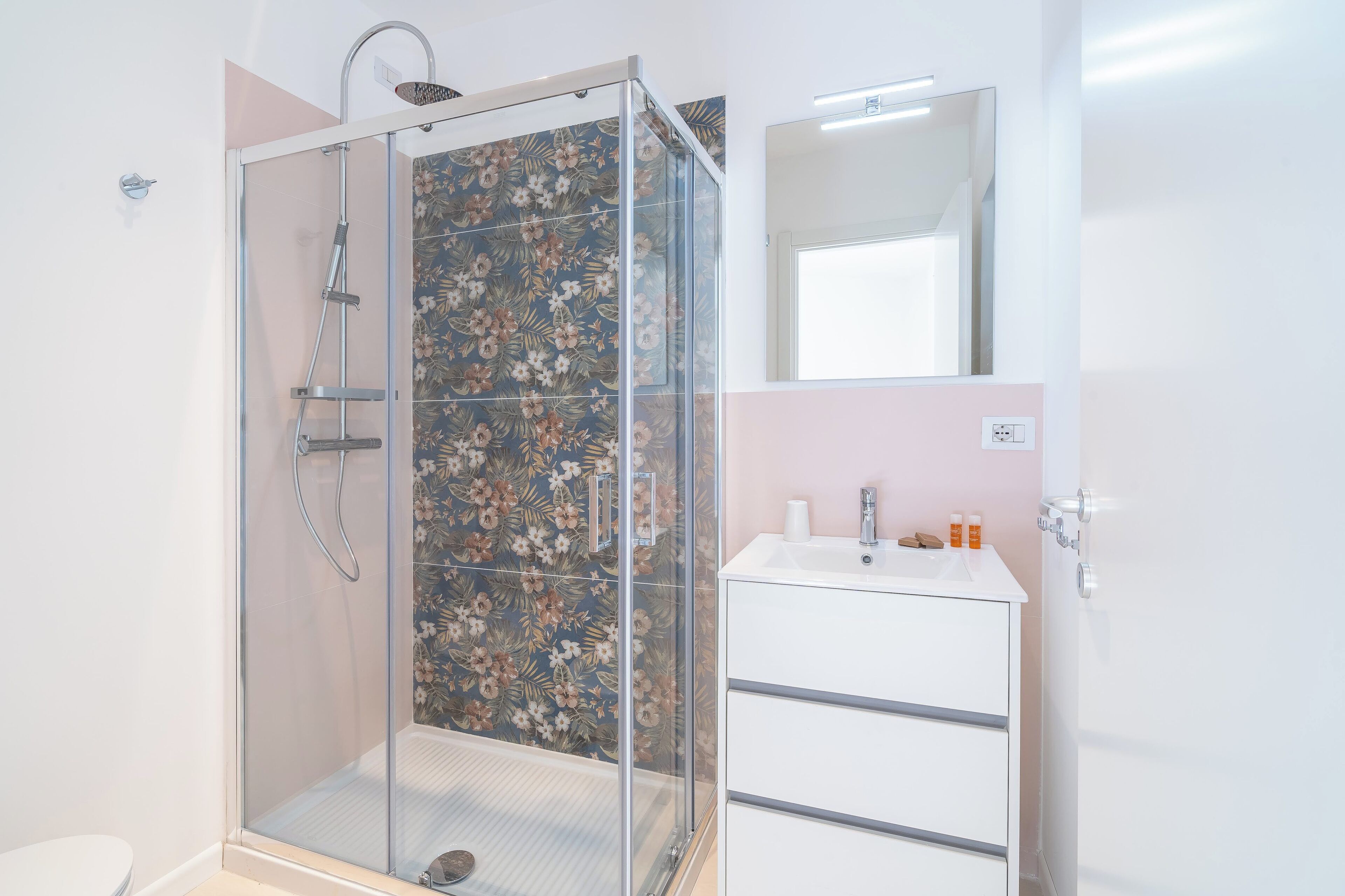 Un baño moderno con ducha de vidrio, un lavamanos blanco y un espejo encima.
