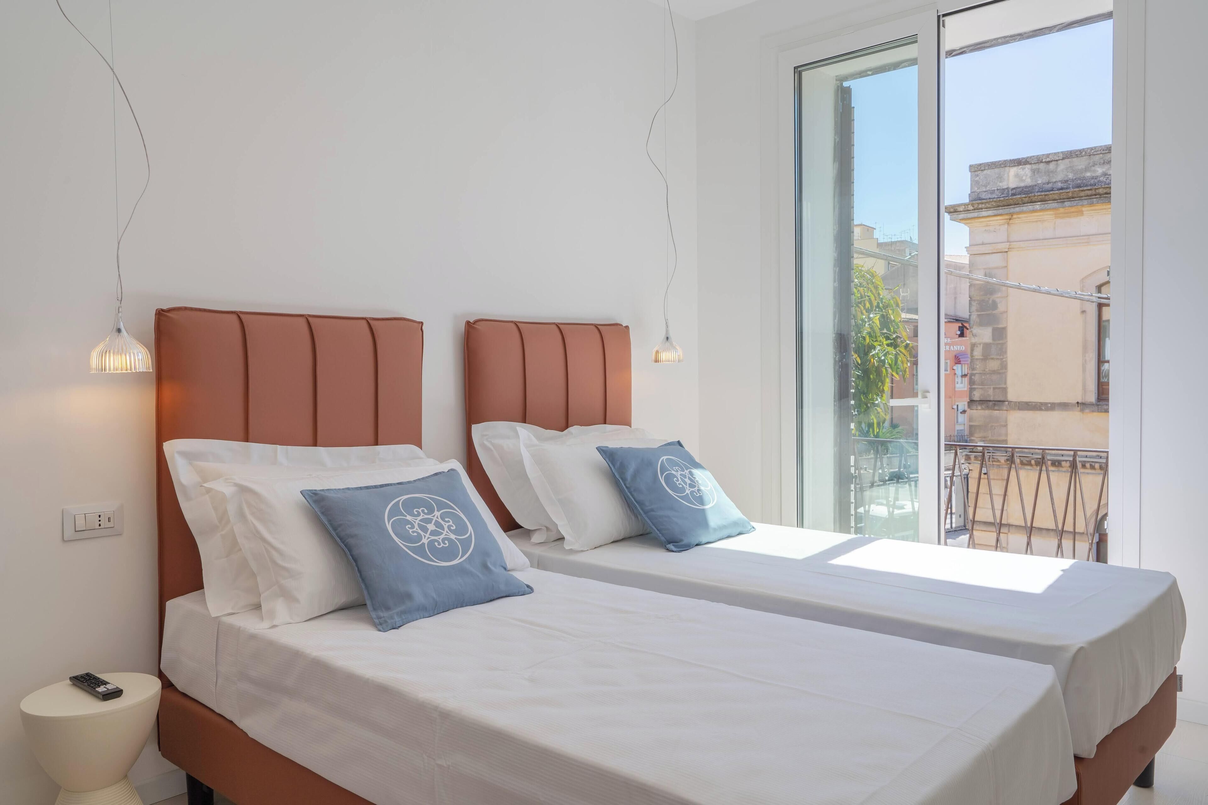 Habitació d'hotel amb dos llits, cada un amb capçalera i almoades, una taula de nit i una finestra amb vista a l'exterior.