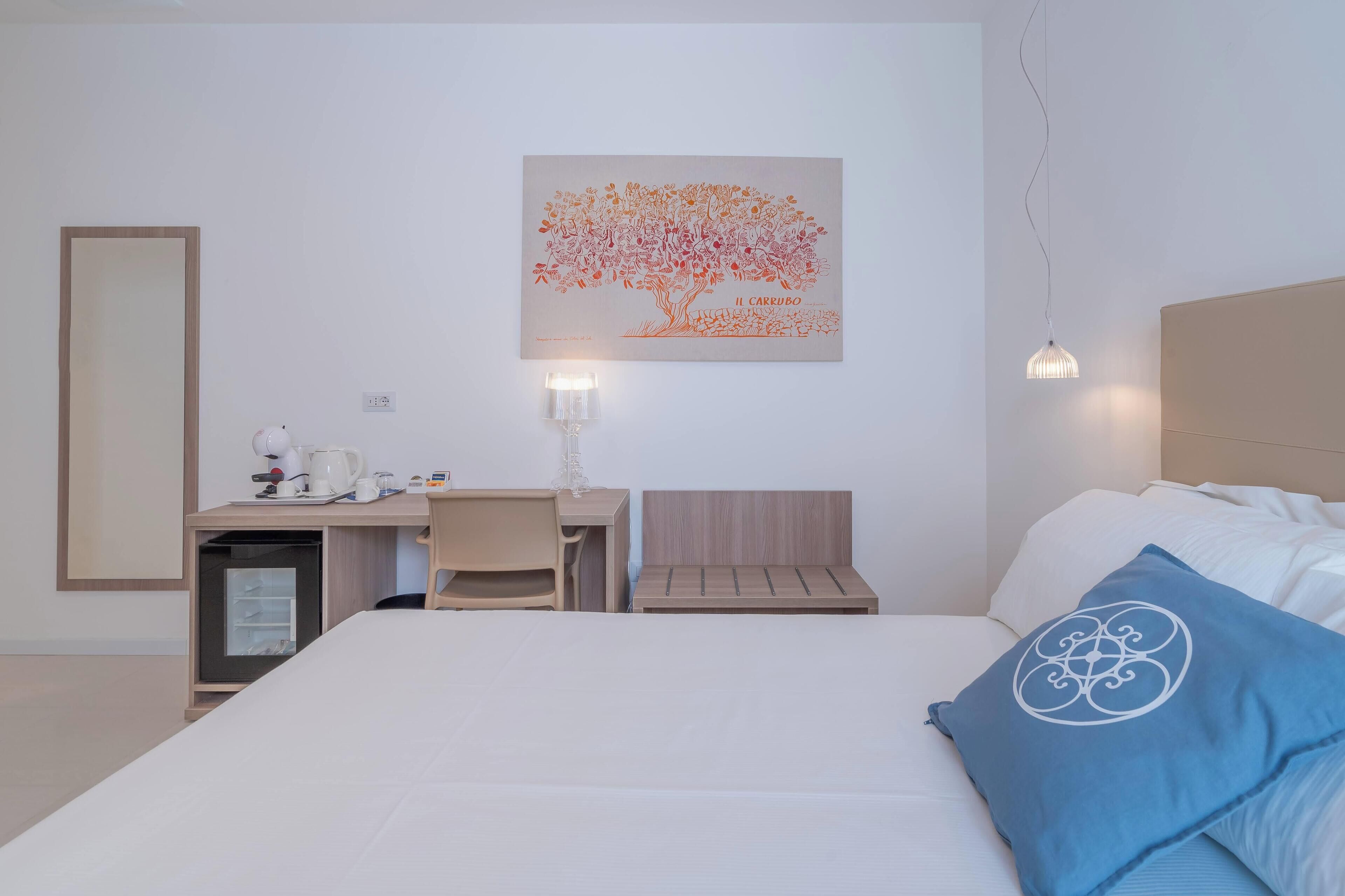 Ein Hotelzimmer mit Bett, Schreibtisch, Stuhl, kleinem Kühlschrank und einem Wandbild.