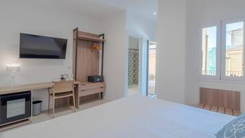 A modern hotel room with a bed, a desk with a computer, a TV, and a wardrobe.