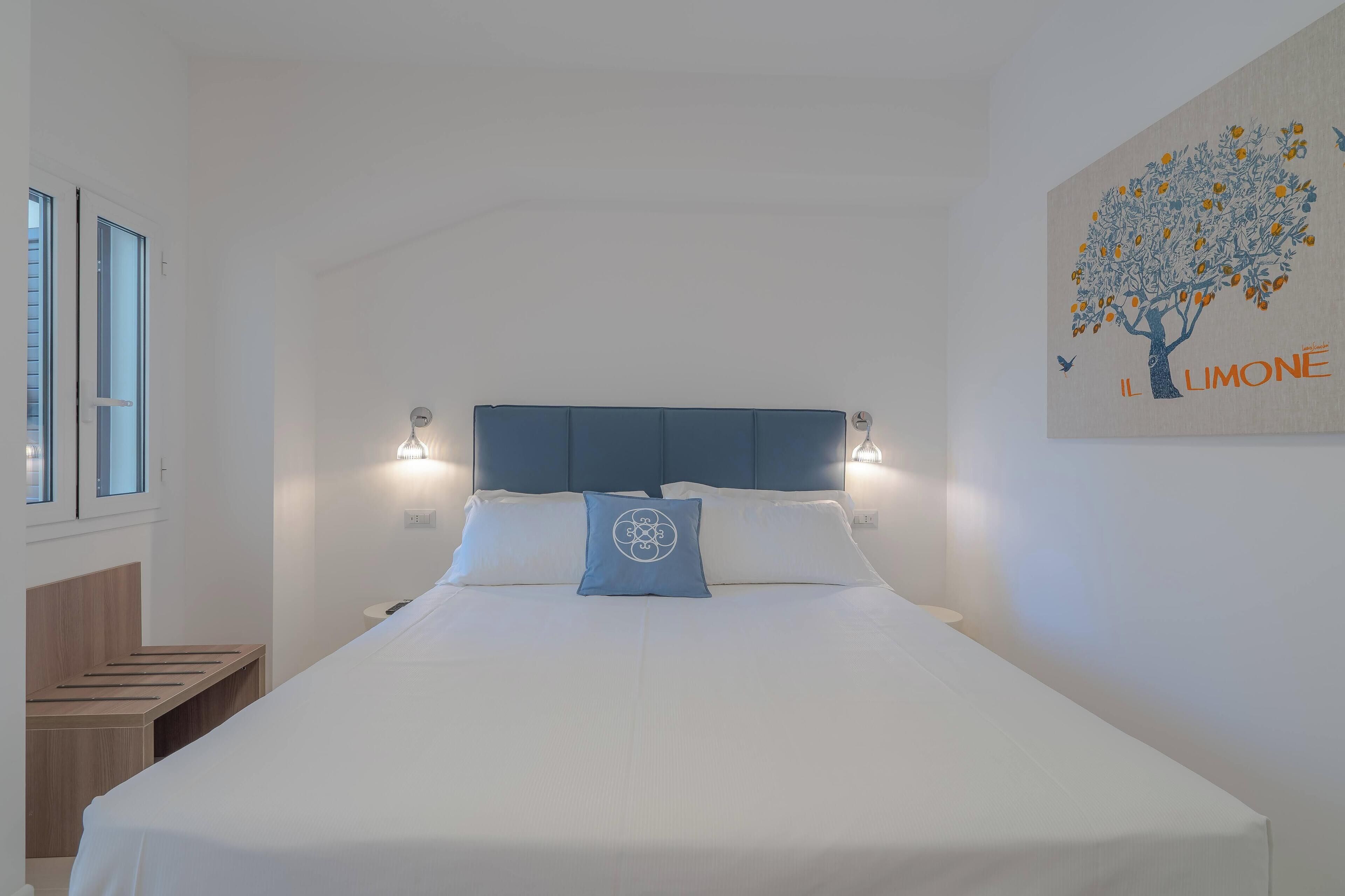 Ein ordentlich bezogenes Bett mit blauem Kopfkissen, einem Kopfteil und Wandleuchten.