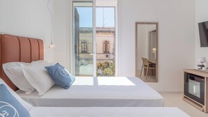 Une chambre avec un lit, un bureau, une télévision et un balcon donnant sur des immeubles.