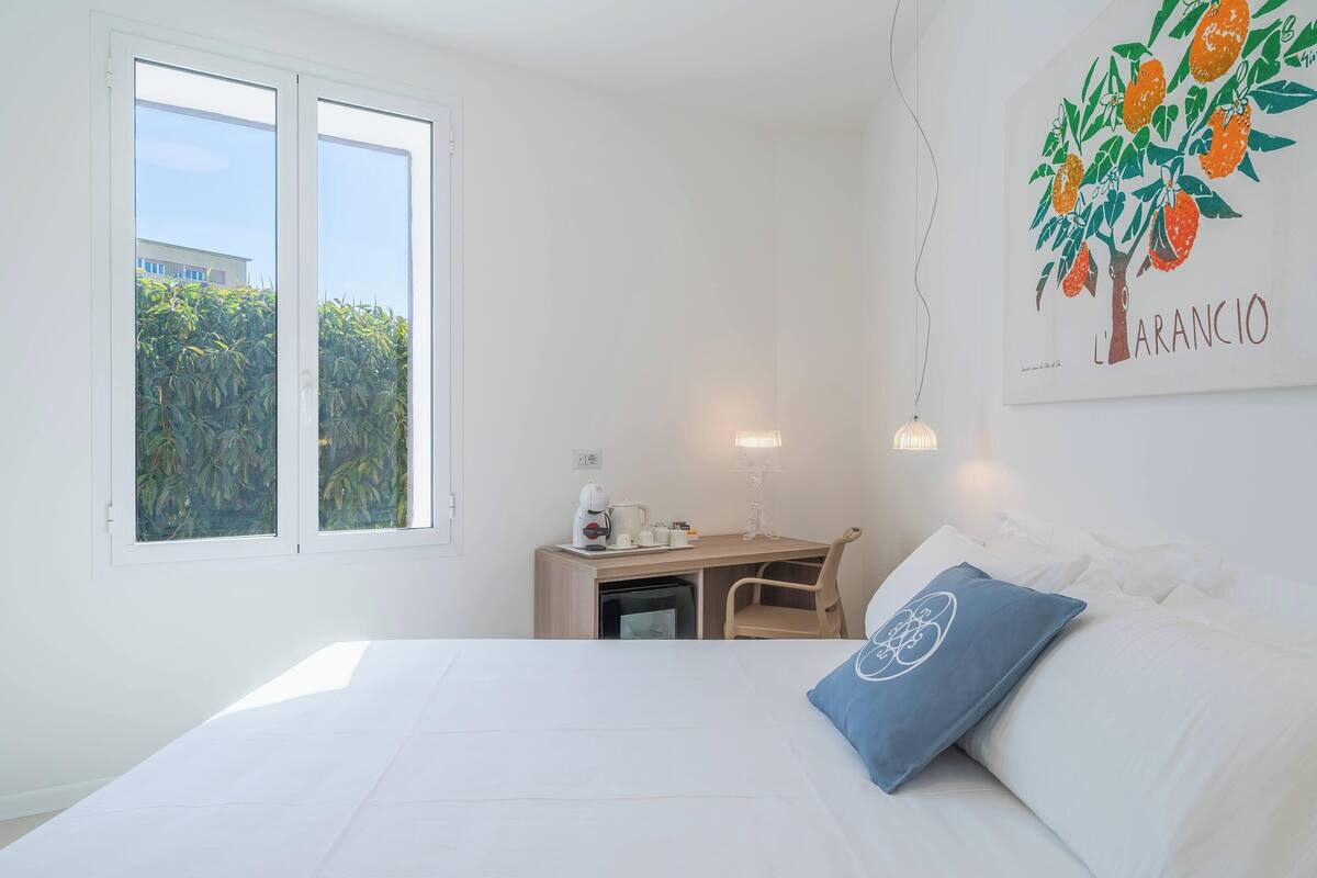 Ein Hotelzimmer mit Bett, Schreibtisch, Stuhl, Fenster und einem Wandbild.