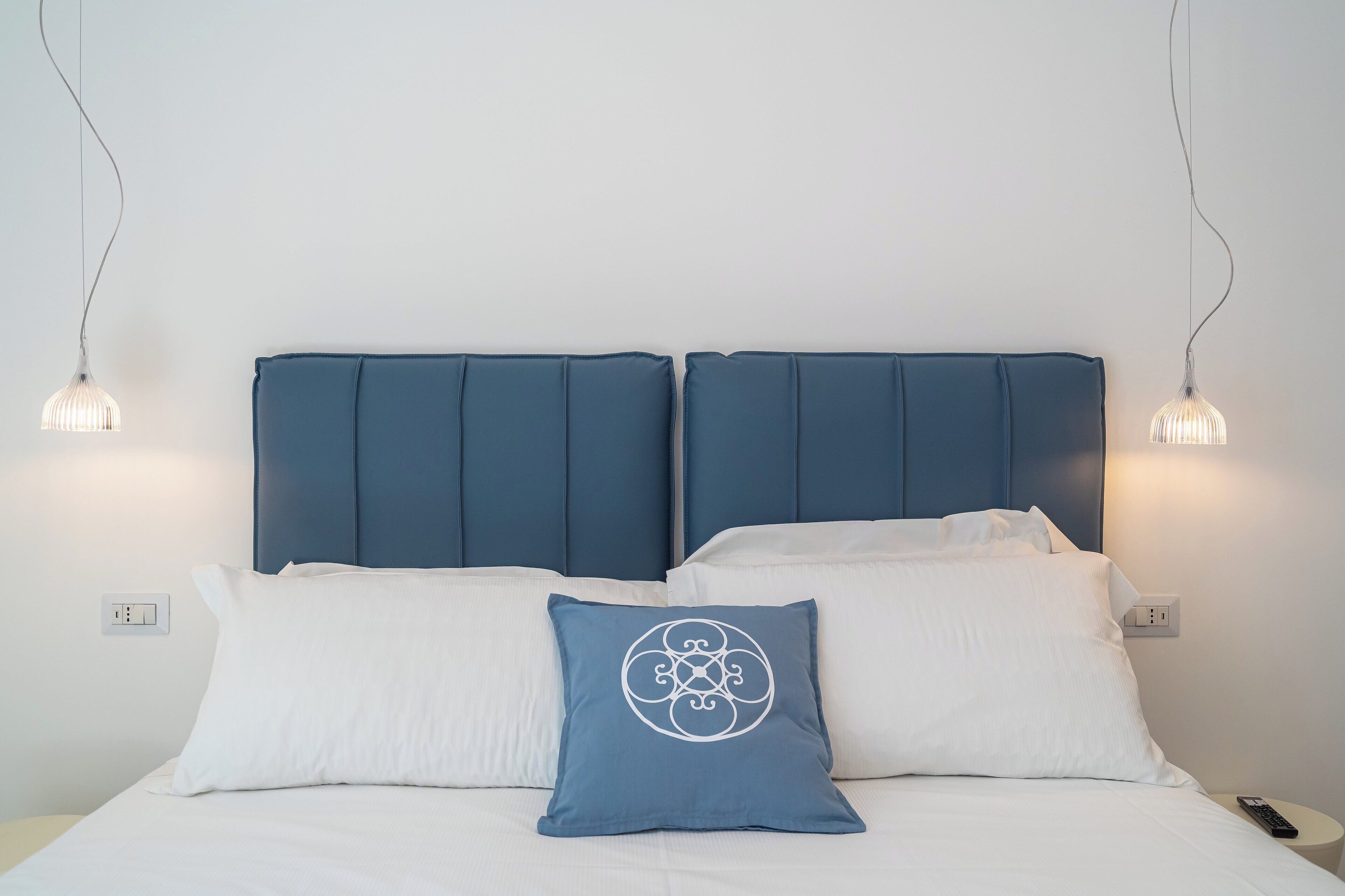 Un lit avec une tête de lit bleue, des oreillers blancs et un coussin décoratif à motifs géométriques.