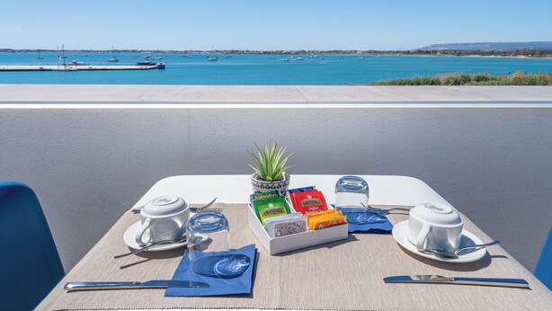 Une table dressée pour deux personnes, avec vue sur la mer et des bateaux en arrière-plan.