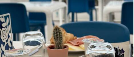 A table with croissants and a cactus, a plate with food, and a view of the sea.