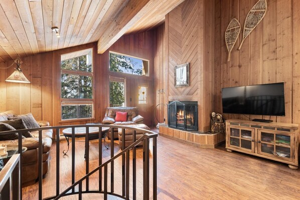 A cozy cabin interior with a fireplace, a TV, and a wooden deck.