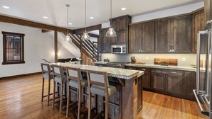 A modern kitchen with dark wooden cabinets, a central island with bar stools, stainless steel appliances, and pendant lighting.